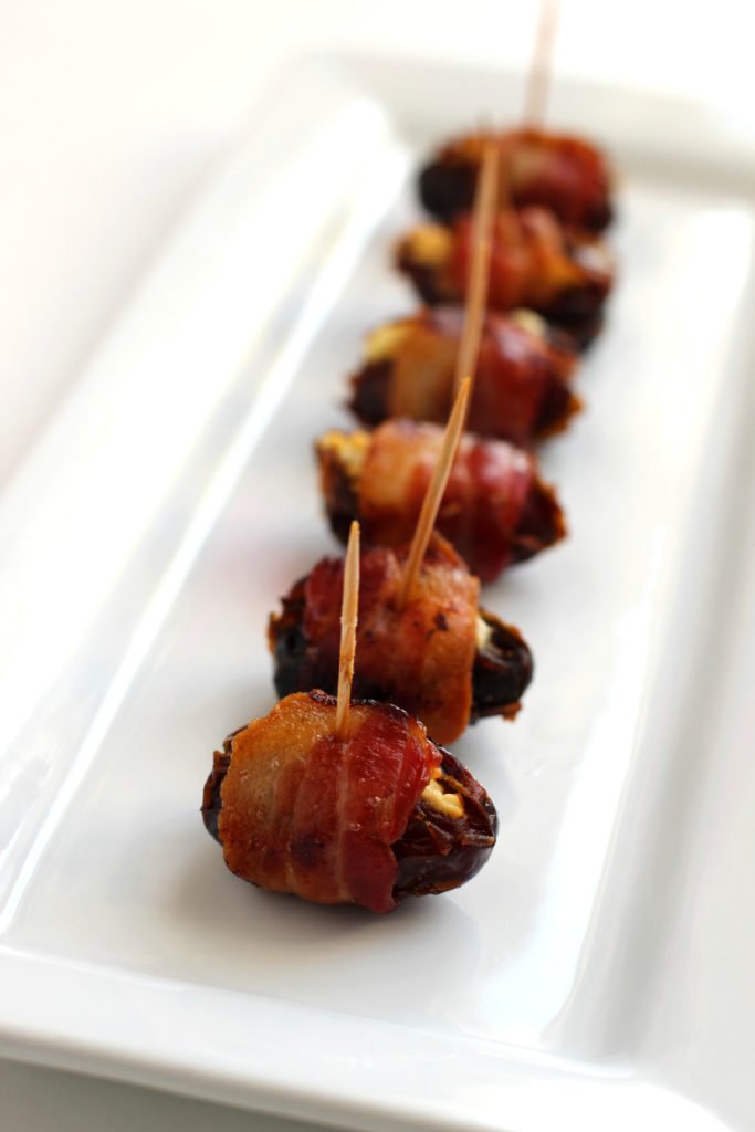 bacon wrapped dates stuffed with goat cheese on a white platter
