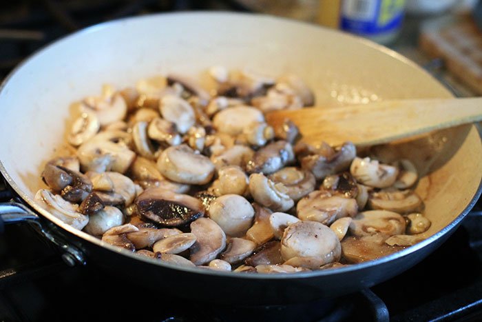 mushrooms cooking stirred in pan with wooden spoon