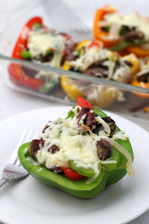 Baked Keto Philly Cheesesteak Stuffed Peppers on table with serving opjn a white plate in foreground