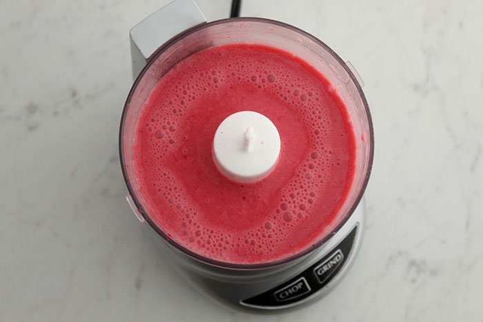 frothy pink liquip in blender over head view on white marble table Raspberry Chocolate Chia Pudding