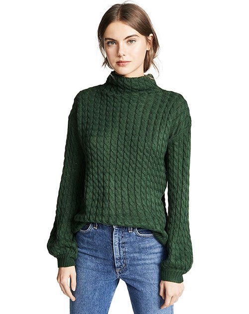 model in hunter green cable knit long sleeve turtleneck with blue jeans