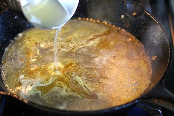 tumeric lemon skillet chicken pouring chicken broth in a hot skillet