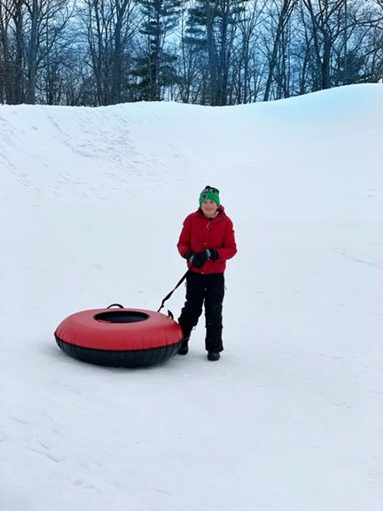 boy with red coate and green hat and snow tube