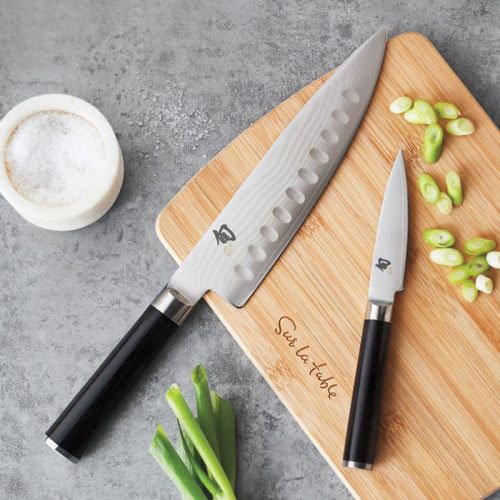 chefs knives on wooden cutting board with chopped green onions on grey counter top
