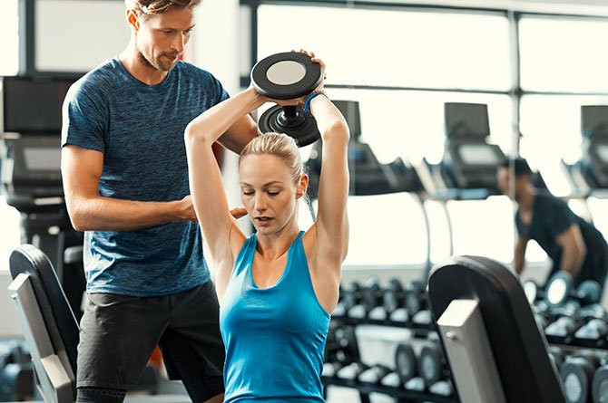 personal trainer spotting woman overhead dumbbell fountainof30