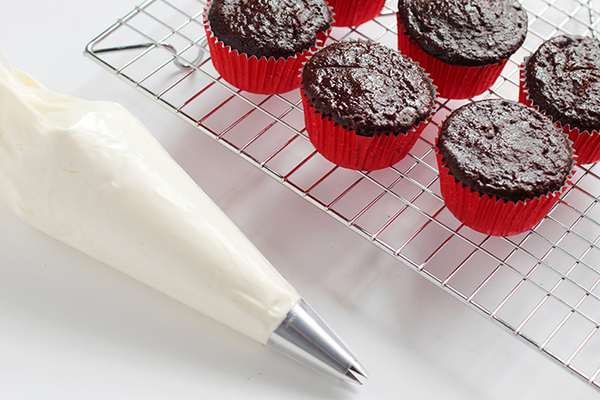 frosting in piping bag with chocolate cupcakes on rack fountainof30