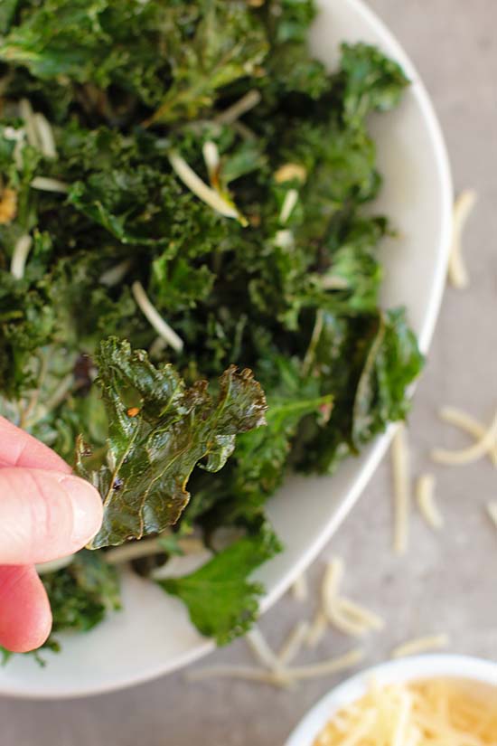 hand lifting a kale chip over bowl fountainof30