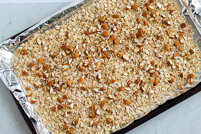 oats and almond slices in a cookie sheet for granola bars fountainof30