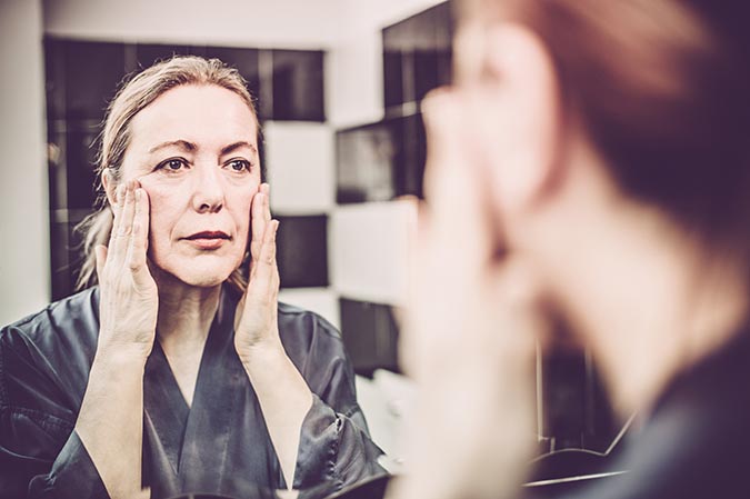 woman thinning skin applying face cream in mirror